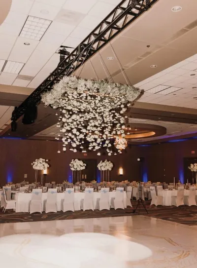 Elegant ballroom reception with white floral chandelier above a polished dance floor and draped banquet tables