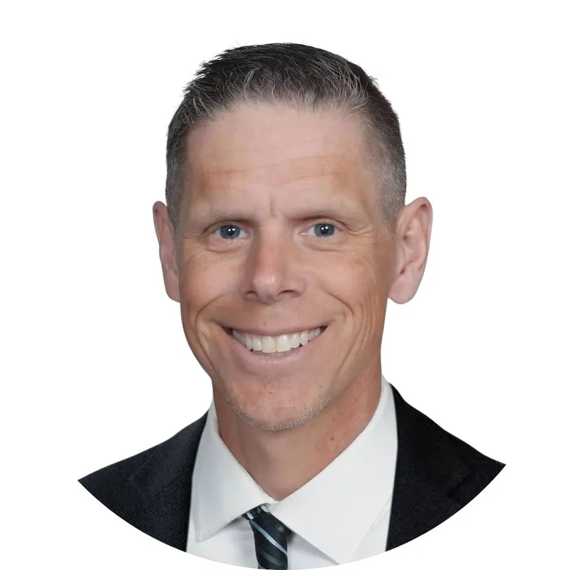 Smiling man with short gray-brown hair wearing a dark blazer and striped tie