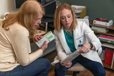 A woman in a white lab coat reviews a pamphlet with a seated patient in jeans