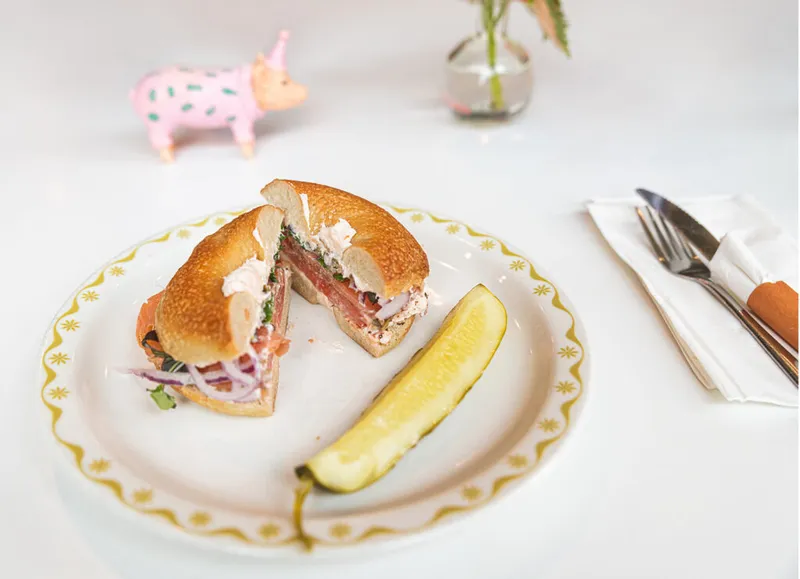 Halved bagel sandwich with cream cheese and salmon beside a pickle spear on a gold-rimmed plate