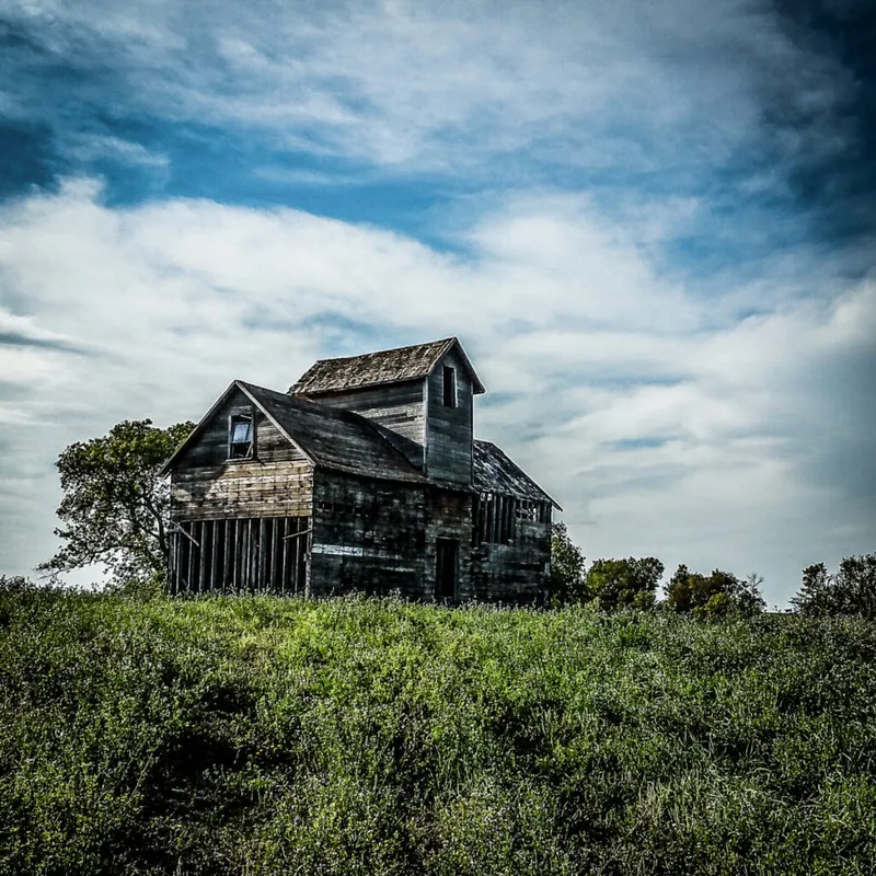 Weathered wooden barn on a grassy hill under a dramatic cloudy sky