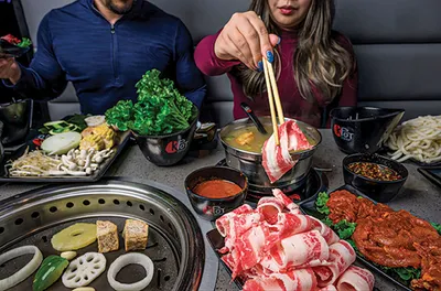 Two diners cooking sliced beef and vegetables at a hot pot table