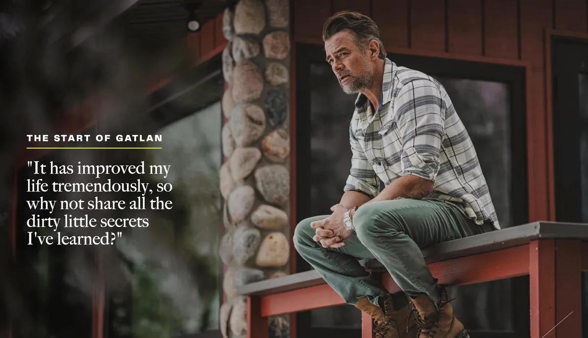 Man with gray beard in plaid shirt and green pants sits pensively on a railing outside a rustic building