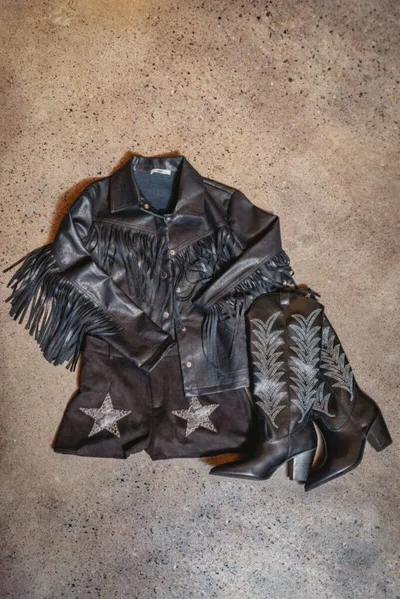 Black fringed leather jacket with star embroidery laid flat beside embroidered cowboy boots