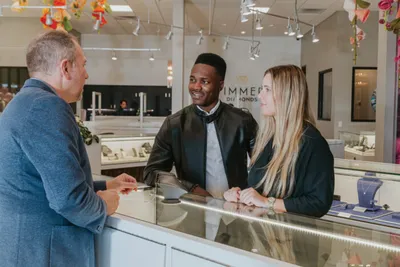 Two customers chat with a jewelry store associate at a glass display counter
