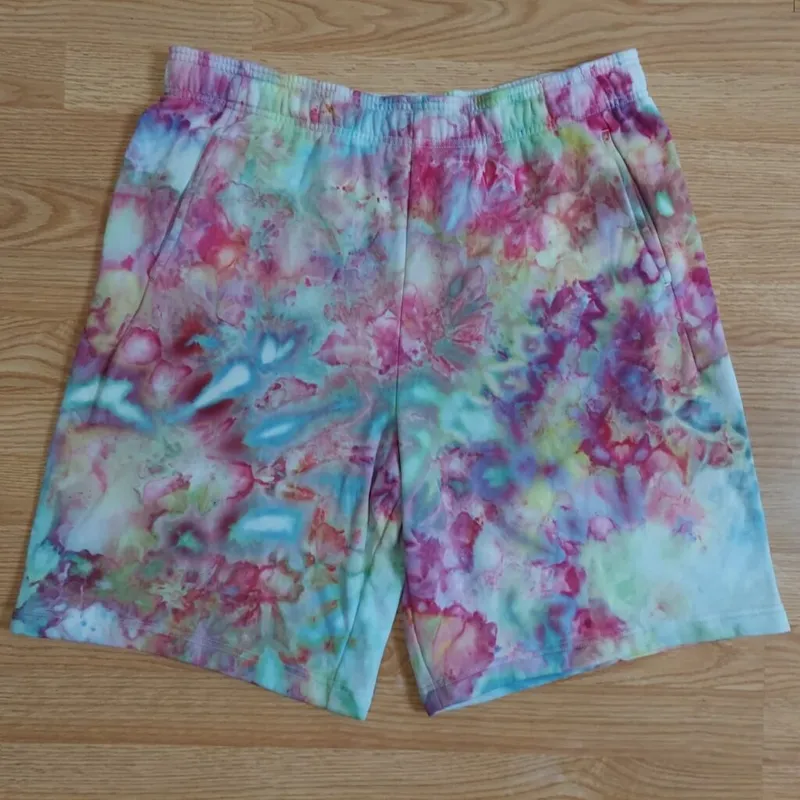 Elastic-waist shorts laid flat on wood surface with pastel ice-dye pattern in pink, teal, and purple