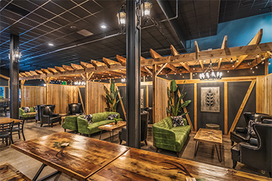 Brewery interior with green velvet sofas, rustic wood beam pergola, and warm Edison lighting