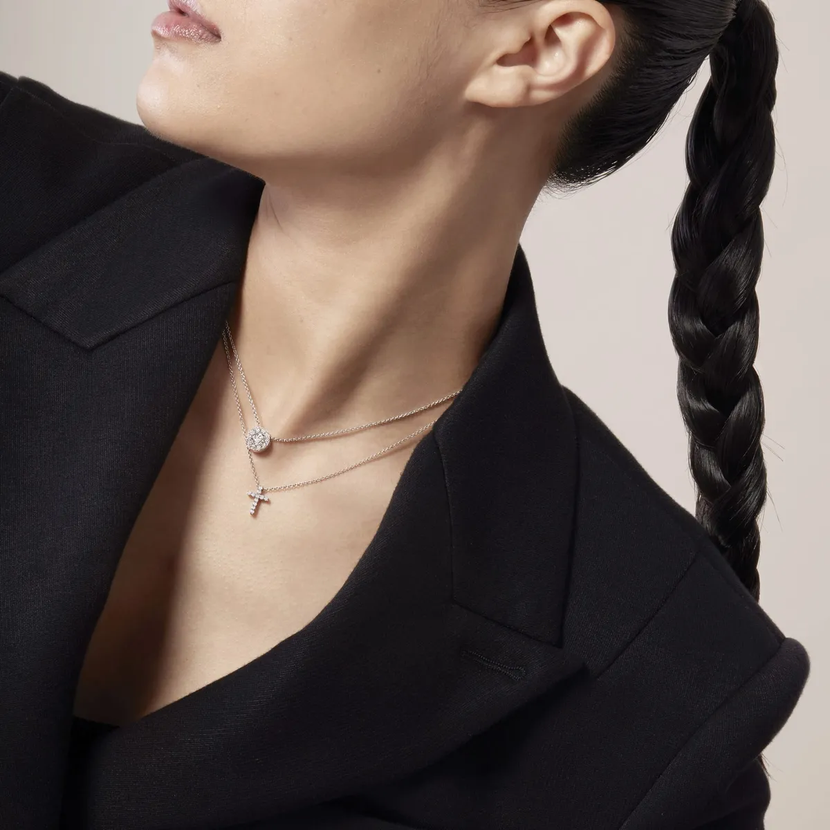Woman in black blazer wearing layered silver necklaces with a cross and circular pavé pendant