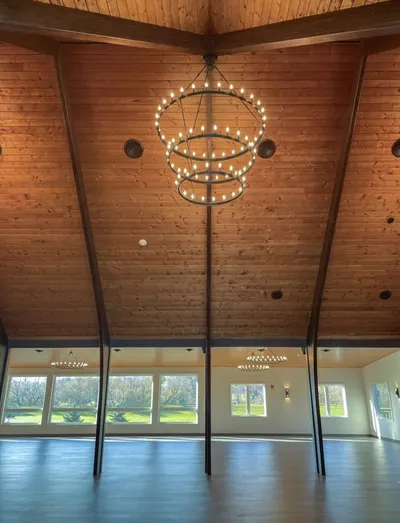 Airy event hall with vaulted wood ceiling, two-tiered ring chandelier, and tall windows overlooking greenery