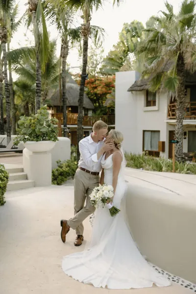 Bride and groom kissing outdoors at a tropical resort, surrounded by palm trees