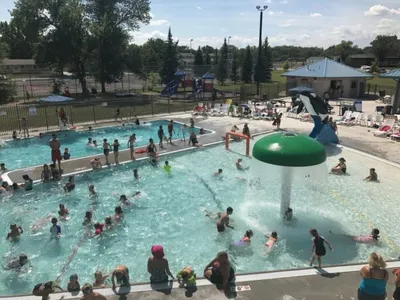 Crowded outdoor public pool with a mushroom fountain and waterslide on a sunny day