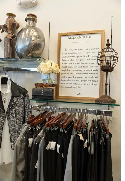 Clothing rack below a glass shelf holding decorative vases and a framed Maya Angelou quote