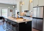Renovated kitchen with dark island, white cabinets, and stainless steel refrigerator