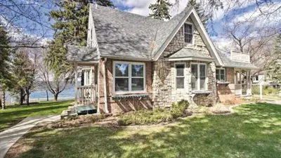 Stone and brick cottage-style house with steep gabled roof near a lake