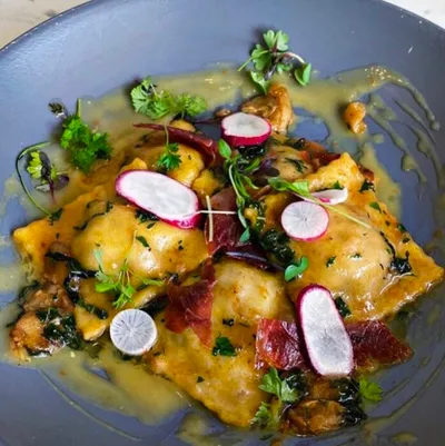 Ravioli in herbed broth topped with sliced radishes and fresh herbs on a blue plate
