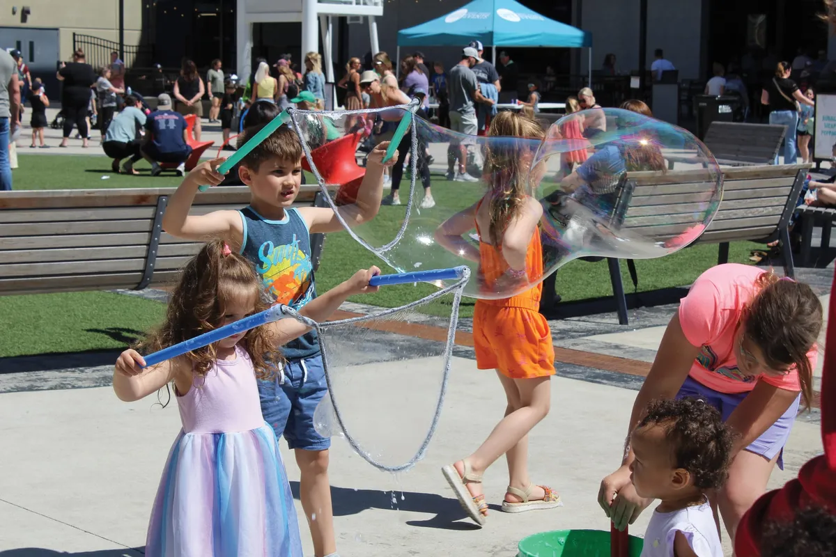 Children making giant soap bubbles with wands at an outdoor community event