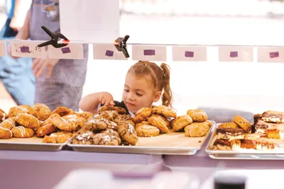 Young girl leaning over trays of assorted pastries and donuts at a market stall