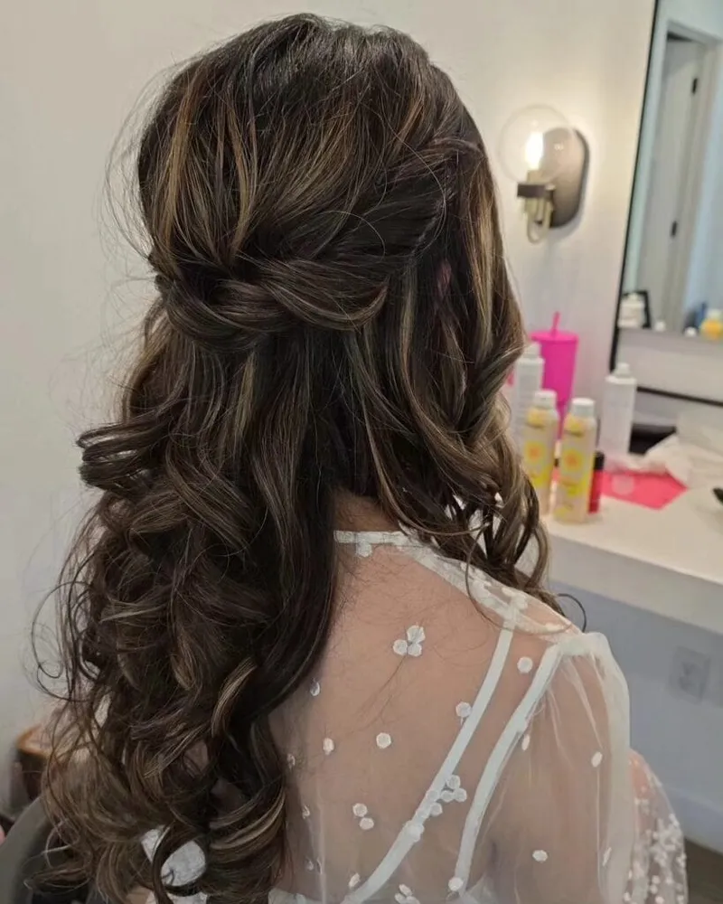 Back view of a half-up twisted hairstyle with long dark curly hair and highlights