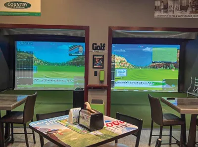 Two golf simulator screens side by side in an indoor lounge with tables and chairs