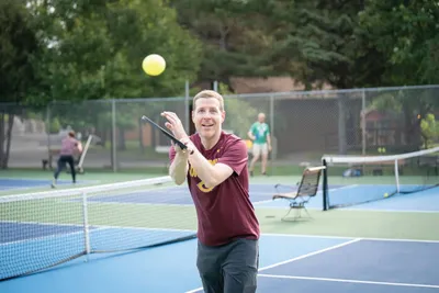 Smiling man hitting a tennis ball on a blue outdoor court