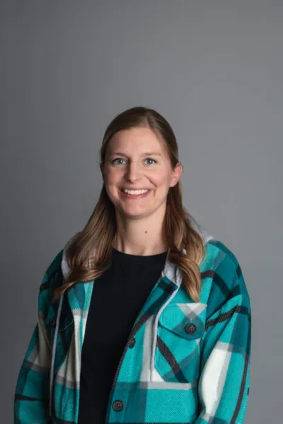 Smiling woman with long brown hair wearing a teal plaid flannel shirt over a black top