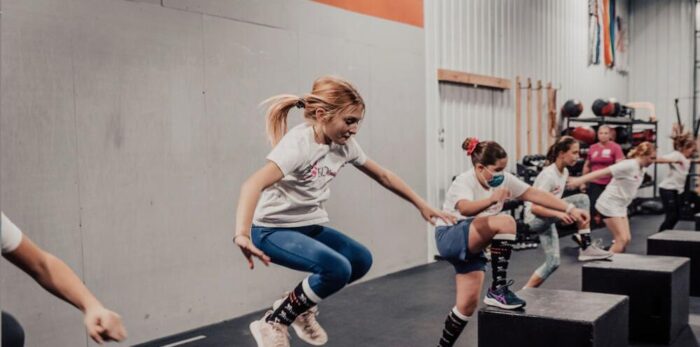 Girls doing box jumps in a gym during a group fitness session
