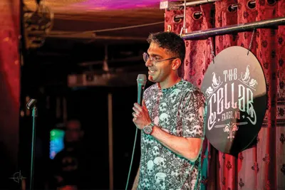 Man in patterned shirt speaks into a microphone on a dimly lit stage at The Cellar