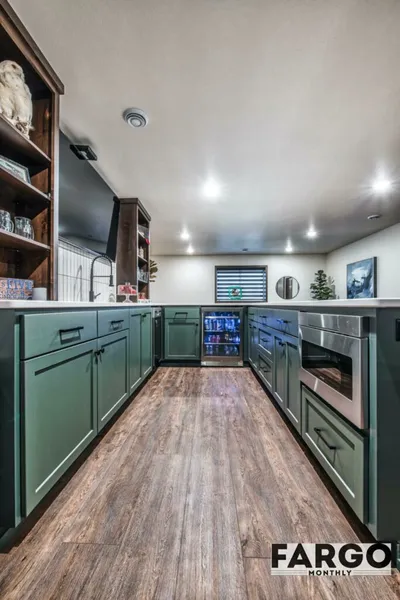 Galley-style kitchen with green lower cabinets, wood-look flooring, and a beverage fridge
