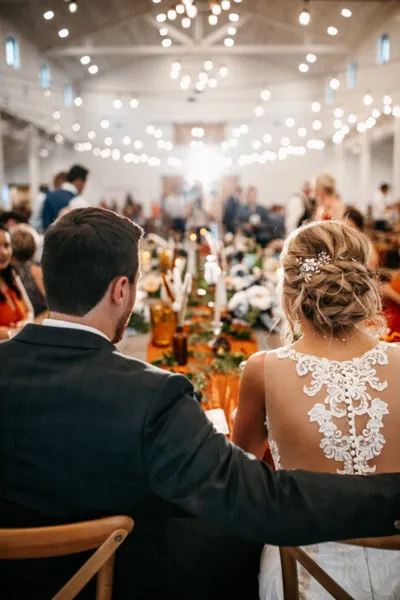 Bride and groom seen from behind at a candlelit wedding reception with string lights