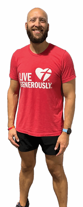 Smiling bald man with beard wearing a red 'Live Generously' T-shirt and black shorts