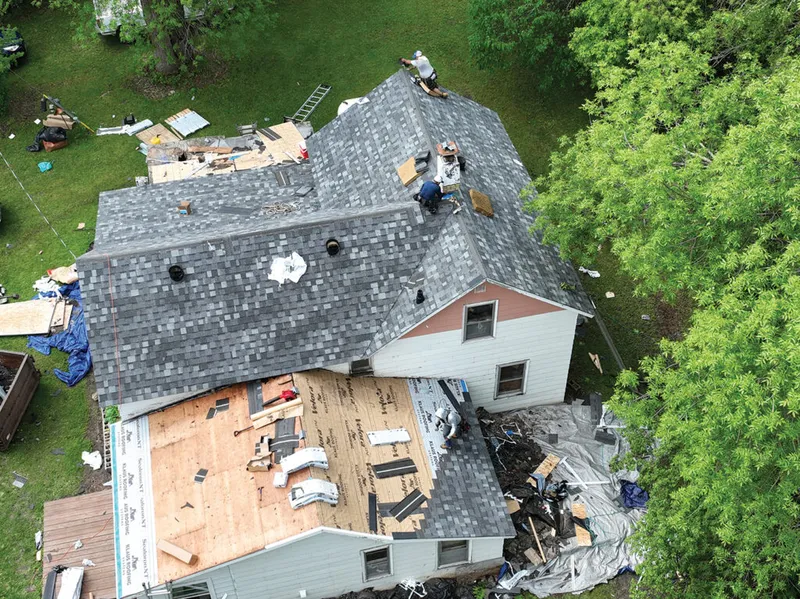 Aerial view of workers replacing shingles on a residential roof mid-renovation