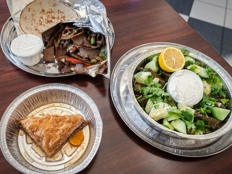 Gyro wrap, cucumber salad with dolmas and tzatziki, and baklava on foil trays