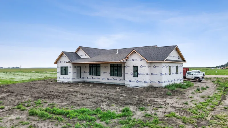 Single-story home under construction wrapped in house wrap, set on a rural lot with flat open fields behind