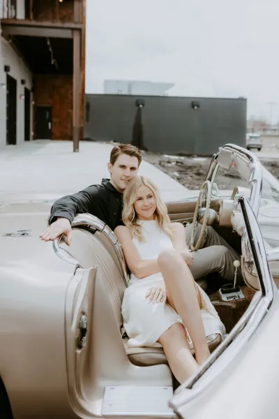 Couple sitting together in a cream vintage convertible outdoors
