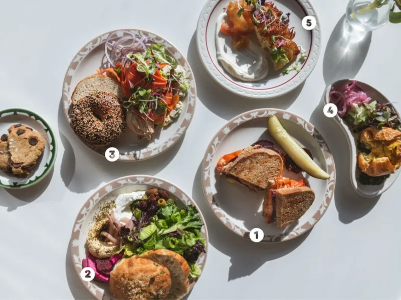 Overhead spread of five numbered plates featuring bagels, sandwiches, salads, and pastries on a white surface