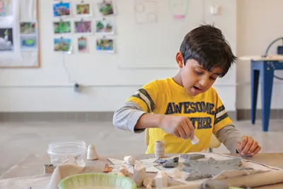 Young boy in yellow shirt sculpting with clay at an art museum workshop table