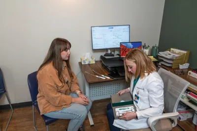 A patient and a white-coated clinician review materials together in a small medical office