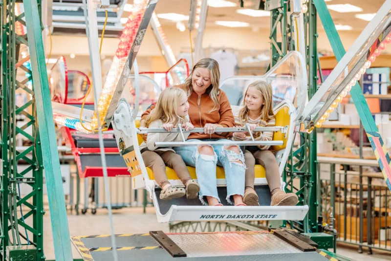 Woman and two young girls laughing on an indoor Ferris wheel gondola marked North Dakota State