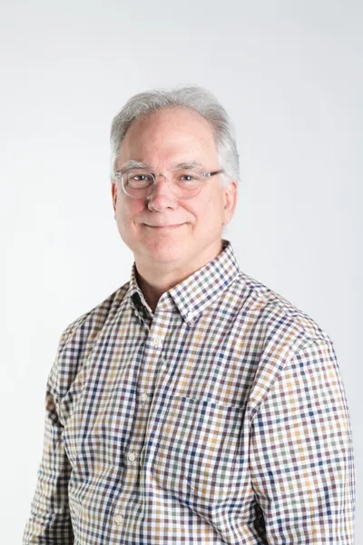 Older man with gray hair and glasses smiling in a plaid button-up shirt