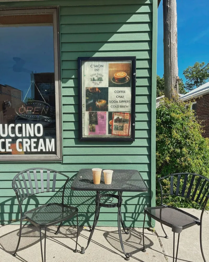 Two iced drinks on a black patio table outside a green-sided café with a menu sign