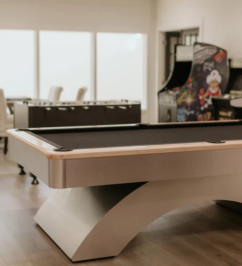 Modern pool table with black felt in a game room with foosball table and arcade cabinet