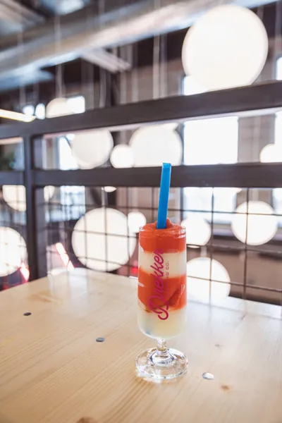 Layered strawberry cream drink with a blue straw in a tall glass on a wooden table