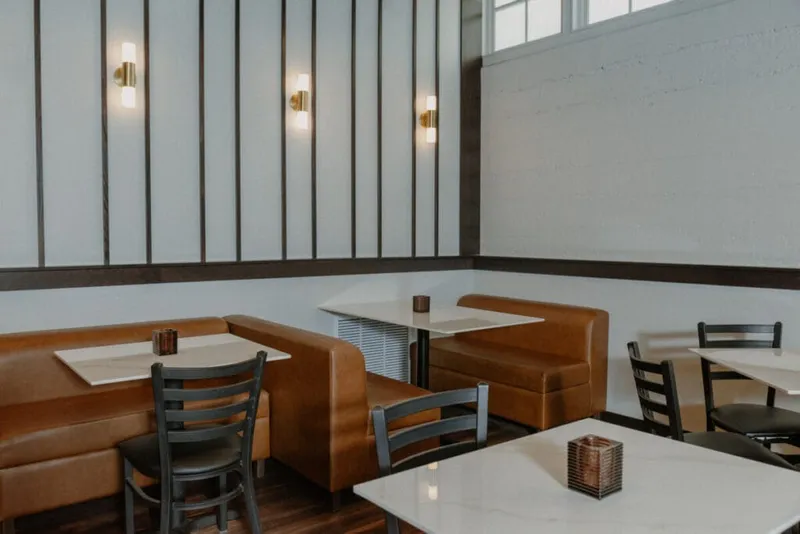 Restaurant dining area with tan leather booths, marble-top tables, and gold wall sconces