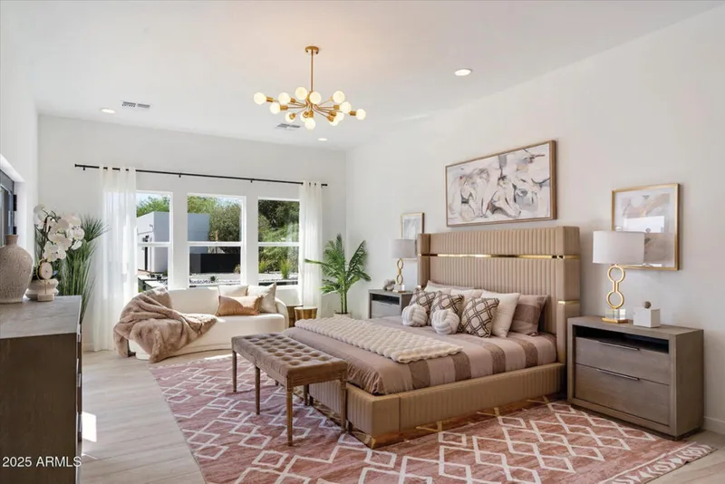 Styled primary bedroom with tall upholstered headboard, gold chandelier, and pink geometric rug