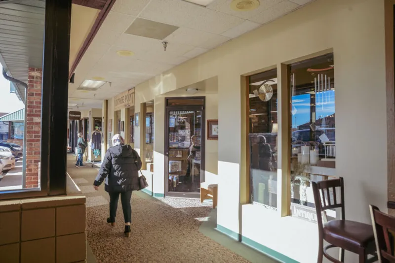 Woman in black puffer jacket walking along a covered strip mall corridor with shops