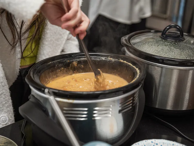 Person stirring creamy orange soup in an open slow cooker beside a second lidded slow cooker
