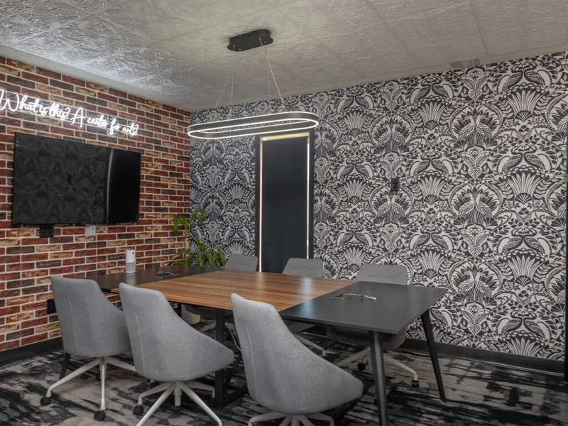 Conference room with bold damask wallpaper, brick wall, neon sign, and oval pendant light above a wood table