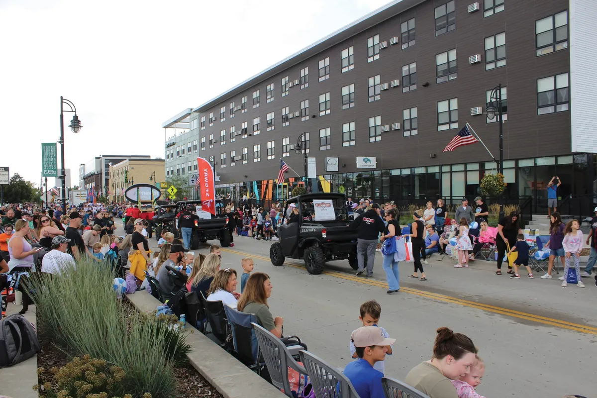 Crowd lining a downtown street for a parade with UTVs and colorful banners