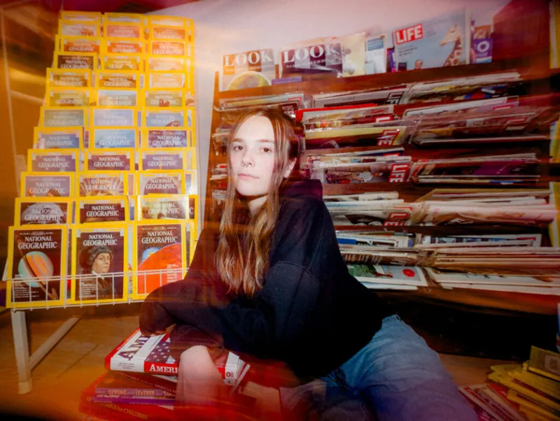 Young woman with long brown hair sitting among racks of National Geographic and Life magazines