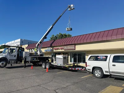 Crane truck lifting an HVAC unit onto a commercial strip mall rooftop
